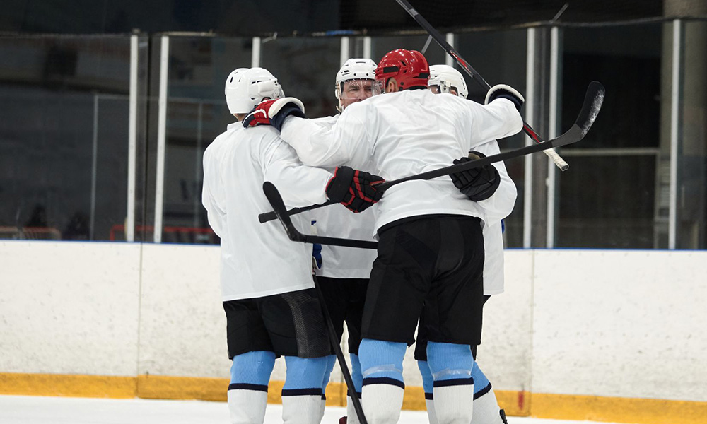 Group of adult hockey players in white jerseys hugging after a goal