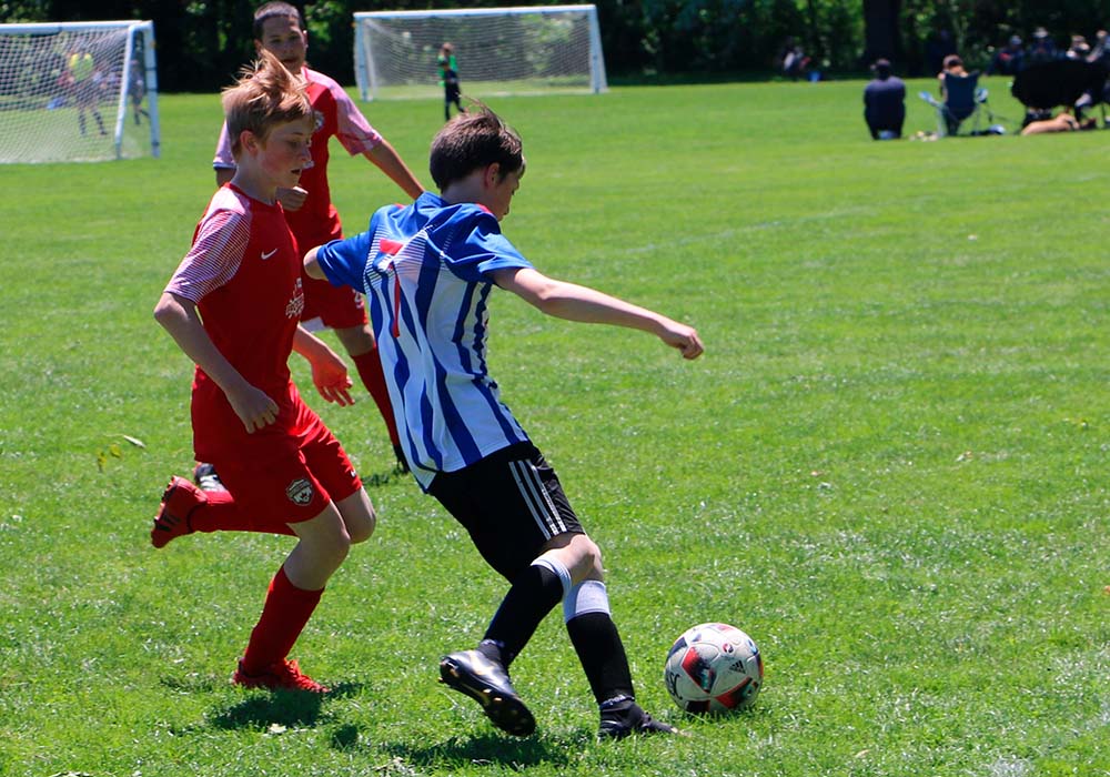 3 kids playing soccer, one kicking a ball