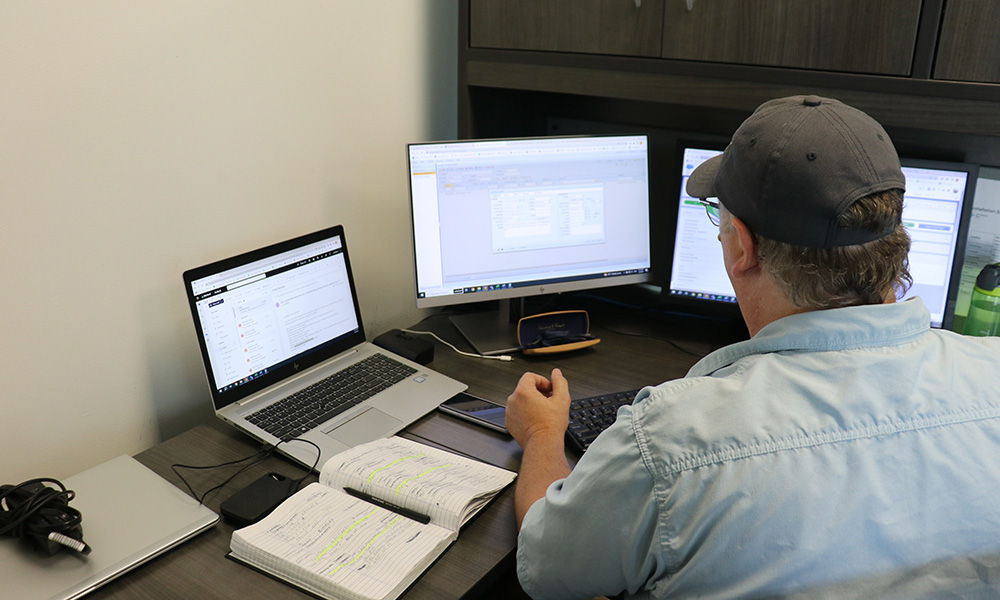 Employee in office looking at 3 computer screens.