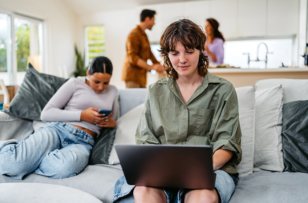 Two teen girls on devices with parents in the background